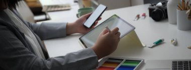 Model akıllı telefon ve tablet üzerinde çalışan profesyonel tasarımcının görüntüsü tasarlanmış malzemelerle beyaz masada. 