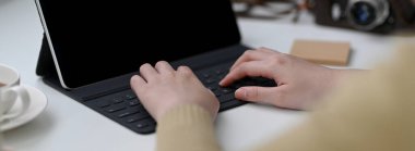 Beyaz masada kahve fincanı ve not defteriyle dijital tablet üzerinde çalışan serbest çalışan kadın.