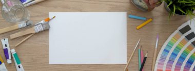 Çizim kağıdı, resim malzemeleri ve ahşap masadaki dekorasyonlarla sanatçı çalışma alanının genel görüntüsü. 