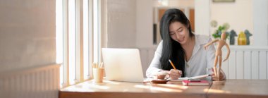 Modern ofis odasındaki ahşap masada dizüstü bilgisayar ve malzemelerle çalışan kadın tasarımcının kırpılmış görüntüsü.