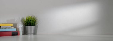 Beyaz duvar arkaplanı olan beyaz masadaki kitaplarla, dekorasyonla ve kopyalama alanıyla basit çalışma alanının görünümünü kapat