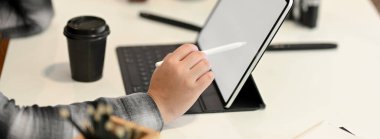 Kadın grafik tasarımcısının yan görüntüsü, kahve fincanı ve çalışma alanı az olan malzemelerle tablet üzerinde çalışıyor.