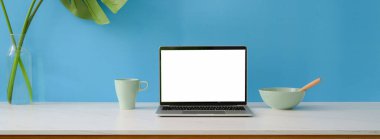 Boş ekran laptop, kahvaltı yemeği ve açık mavi duvarlı mermer masa dekorasyonu ile yaratıcı çalışma alanını kapat