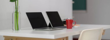 Dizüstü bilgisayarı, dijital tableti, kupası, kamerası, ofis malzemesi ve dekorasyonu olan rahat ofis masasının yan görüntüsü.