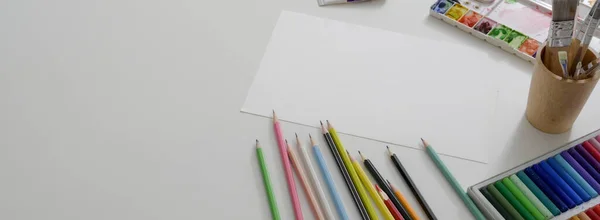 Overhead shot of artist workspace with sketch paper, oil pastels, painting tools and copy space on white desk