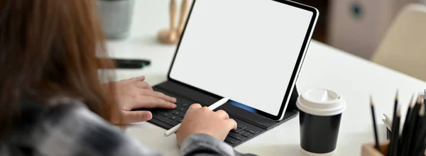 Cropped shot of female graphic designer typing on blank screen tablet on worktable with stationery and coffee cup