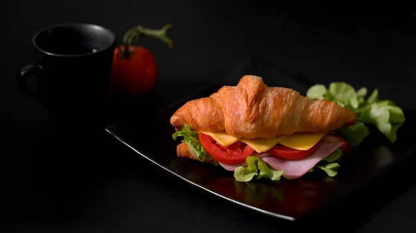 用新鲜的羊角面包三明治火腿和奶酪在黑盘上切好的早餐大餐 — 图库照片