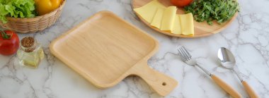 Ahşap tepsi, peynir, sebze, malzeme ve çatal bıçaklı mermer mutfak masası. 
