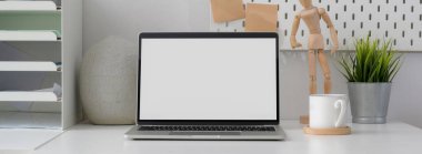 Boş ekran laptop, kahve fincanı ve beyaz masadaki dekorasyonlarla basit ofis masasının görüntüsünü kapat  