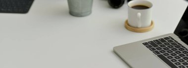 Dizüstü bilgisayar, kahve fincanı, süslemeler ve beyaz masadaki fotokopi alanı ile rahat çalışma alanının görüntüsü.  