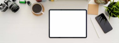 Boş tablet, kahve fincanı ve diğer malzemeleri beyaz masanın üzerinde bulunan en küçük çalışma alanının en üst görüntüsü 
