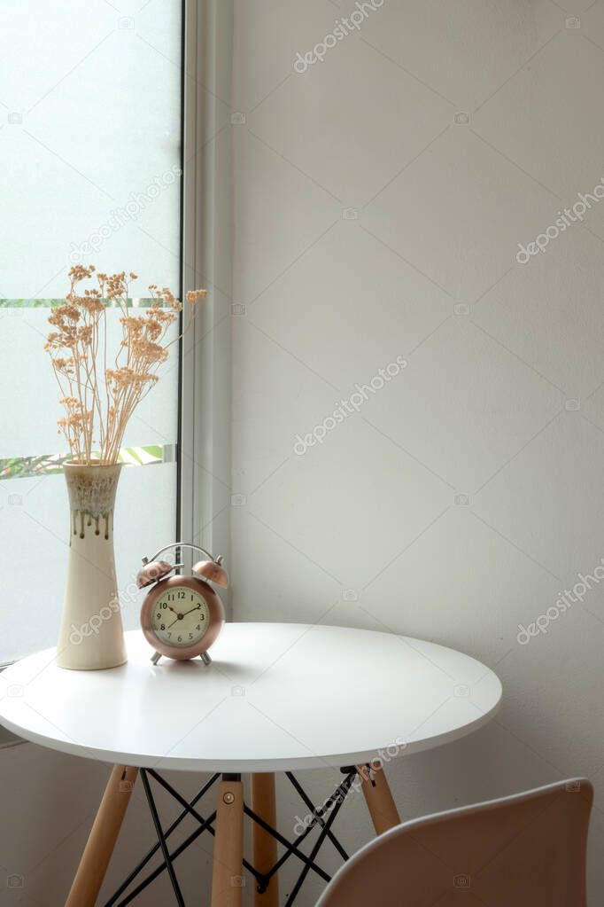 Cropped shot of modern home interior design with flower vase, clock and copy space on white circle coffee table next to window 