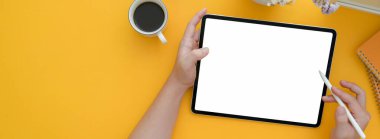 Serbest çalışanın yaratıcı çalışma tabletinde otururken elinde maket tablet tutarken çekilen resmi.