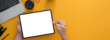 Boş ekran tabletine serbest yazıcının resmi. Stylus, malzemelerle ve kopyalama alanlarıyla birlikte sarı çalışma masasında.