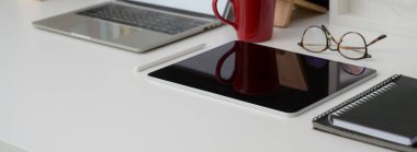 Dijital cihazlar, bardaklar, kupalar ve diğer malzemelerle birlikte beyaz masanın üzerine işlenmiş şık bir resim.   