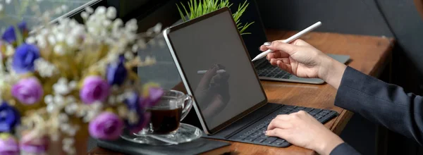 Cropped shot of businesswoman working on mock-up tablet with stylus, coffee cup and decoration on wooden counter bar in coffee shop