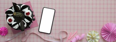 Top view of pink scott pattern background with mock-up smartphone, Black Forest cake, decorations and copy space  clipart