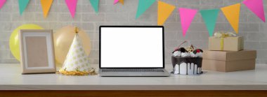 Çevrimiçi doğum günü partisi konsepti boş ekran dizüstü bilgisayar, pasta, parti şapkası ve beyaz masadaki hediye kutuları 