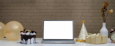 Online doğum günü partisi konsepti. Sahte dizüstü bilgisayarı, Kara Orman pastası, hediye kutusu, balonlar ve beyaz masasında parti şapkası. 