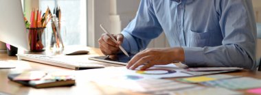 Tahta çalışma masasında otururken, dijital tablete çizim yapan grafik tasarımcısının kırpılmış görüntüsü 