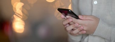 Bokeh arka planında dururken elinde akıllı telefon tutan bir kızın yakın görüntüsü 