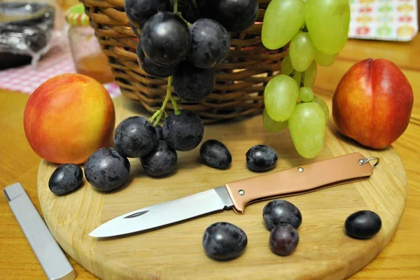 Folding knife stainless steel blade and fresh organic ripe fruits peaches grape natural gourmet product dessert wood background