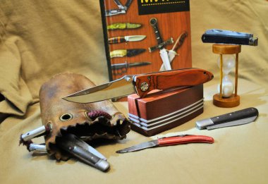 Katlanmış antika bıçaklar, paslanmaz çelik, parlak bıçak, doğal ahşap saplar, kum saati, eski deri çanta, kahverengi arka plan.