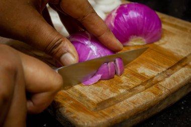 Kırmızı soğanı bıçakla doğrayan bir kadın.