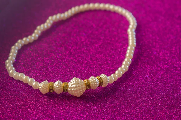 Pearl necklace on a shiny purple background. White colour jewellery.