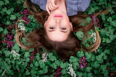 Eli olan güzel bir kız çiçeklerle çimlerin üzerinde yatıyor - doğal güzellik