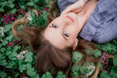 Eli olan güzel bir kız çiçeklerle çimlerin üzerinde yatıyor - doğal güzellik