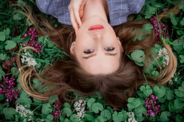 Eli olan güzel bir kız çiçeklerle çimlerin üzerinde yatıyor - doğal güzellik
