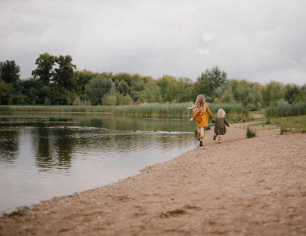 Sarı saçlı iki küçük kız. Kız kardeşler parktaki ördeklerin olduğu bir gölün kıyısında koşuyorlar. - Stok İmaj