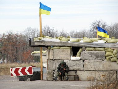VOLNOVAKHA, UKRAINE - OCTOBER, 2014: Ukrainian border guard sitting near the concrete pavement clipart
