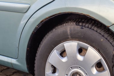 Mavi bir arabanın üzerinde pas var. Eski, yıpranmış metal yüzeyde paslı bir delik. Araç metalinin kazadan dolayı aşınması