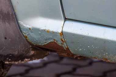 Mavi bir arabanın üzerinde pas var. Eski, yıpranmış metal yüzeyde paslı bir delik. Araç metalinin kazadan dolayı aşınması