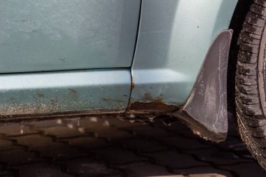 Mavi bir arabanın üzerinde pas var. Eski, yıpranmış metal yüzeyde paslı bir delik. Araç metalinin kazadan dolayı aşınması