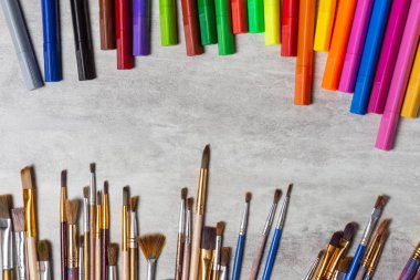Paint brushes and multi-colored markers scattered on the table, drawing tools top view on a gray background, copy space, close-up clipart