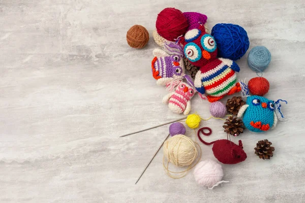 Handmade knitted funny toy owls with skeins of thread and yarn, knitting needles and pins on the table. Close-up and copy space. Hobby and decor. Needlework and children\'s creativity concept