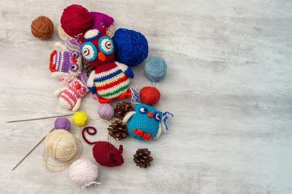 Handmade knitted funny toy owls with skeins of thread and yarn, knitting needles and pins on the table. Close-up and copy space. Hobby and decor. Needlework and children\'s creativity concept