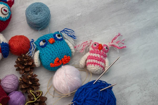 Handmade knitted funny toy owls with skeins of thread and yarn, knitting needles and pins on the table. Close-up and copy space. Hobby and decor. Needlework and children\'s creativity concept