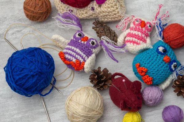 Handmade knitted funny toy owls with skeins of thread and yarn, knitting needles and pins on the table. Close-up and copy space. Hobby and decor. Needlework and children\'s creativity concept