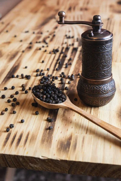 Peppercorn, una cuchara, picadora de especias, en una tabla de cortar de madera — Foto de Stock