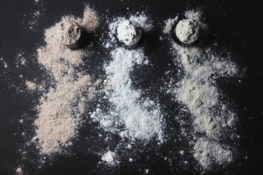 Üç kavanoz dolusu un, glütensiz alternatifler, serpilmiş un, siyah arkaplan.