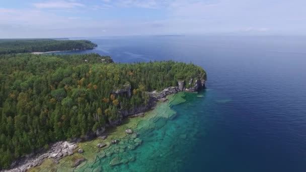 带着松林和清澈的蓝水在半岛上空缓缓飞行的无人机 — 图库视频影像