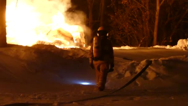 Vyčerpaný hasič odcházející v hlubokém sněhu s plameny hořícími poblíž