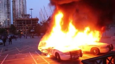 Çevik kuvvet ekipleri göz yaşartıcı gaz atarken iki polis arabası yanıyor.