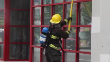 İtfaiyeci mızrak direğini sallıyor ve camları kırıyor.