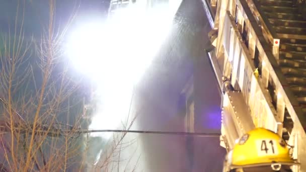 消防士やはしごで夜の建物の屋根に水が飛び散る — ストック動画