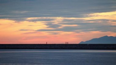 İnsanlar gün batımında denizde yürüyor.